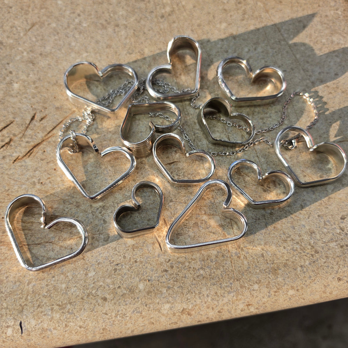 A group of silver heart-shaped wire cutout pendants or charms scattered on a beige stone surface, with some showing attached thin silver chains.