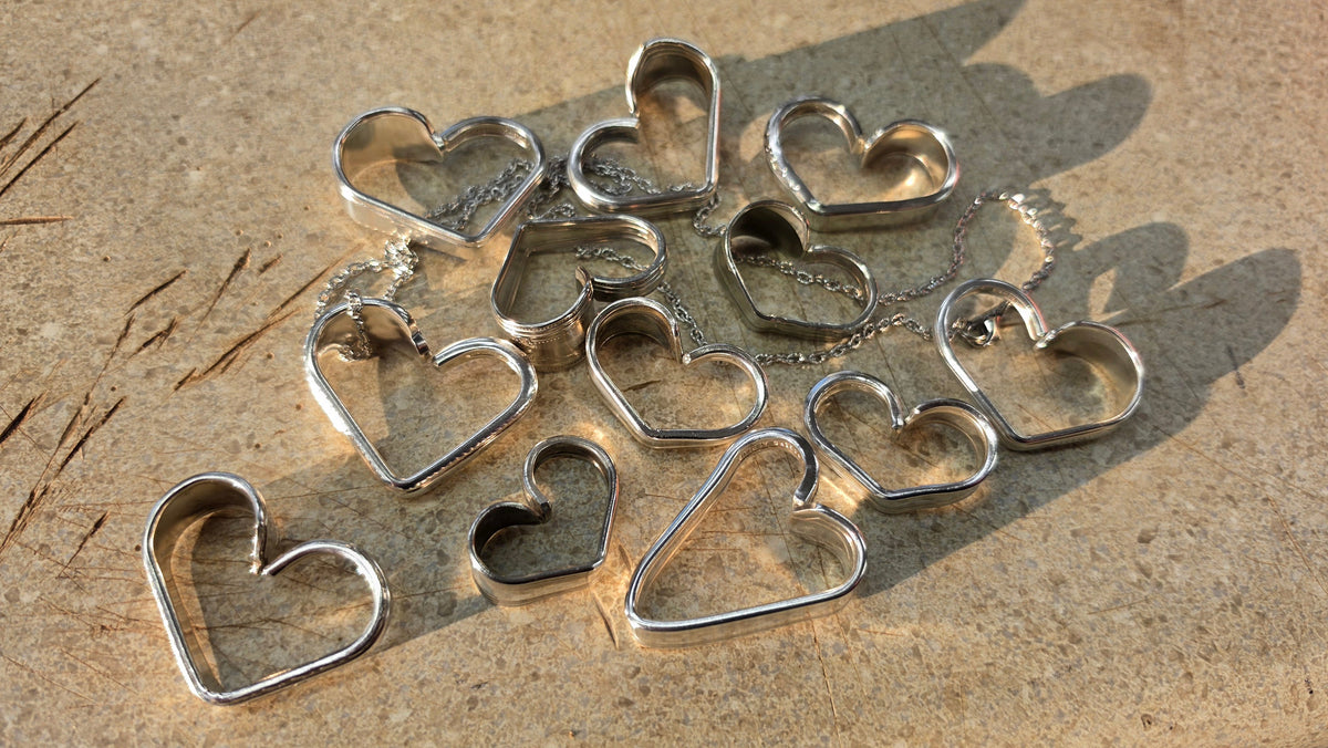 A set of silver metal heart-shaped ring stretchers or stretchers for heart-shaped rings, arranged on a textured beige stone surface.