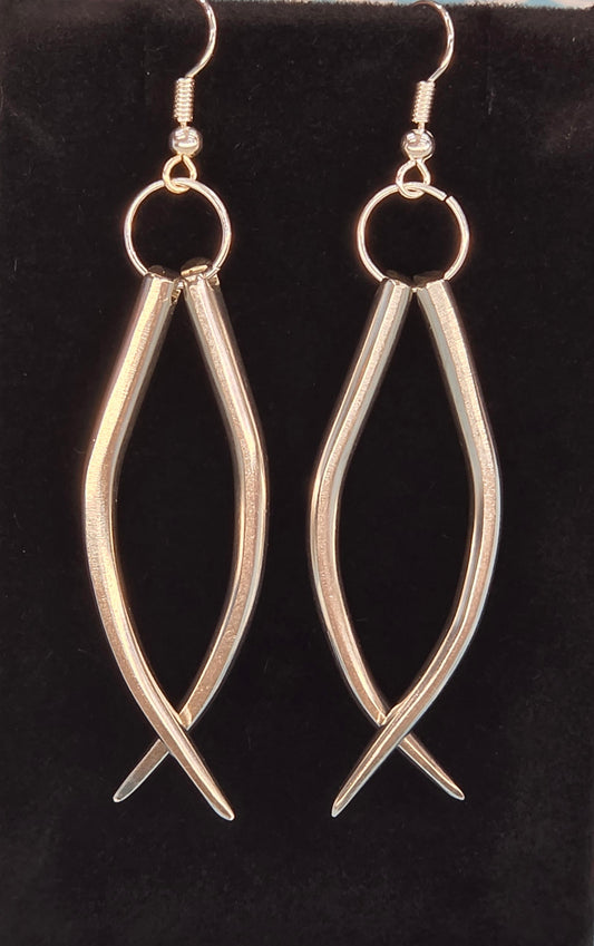A pair of silver-toned fishhook earrings with circular hoops and elongated teardrop-shaped dangling bars, displayed on a black velvet jewelry stand against a blue and white patterned background.